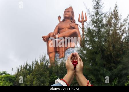 Main de prière de dévot avec des fleurs et dieu hindou flou lord shiva statue à l'image du matin est prise à la Statue de la croyance ou Vishwas Swaroopam nathd Banque D'Images