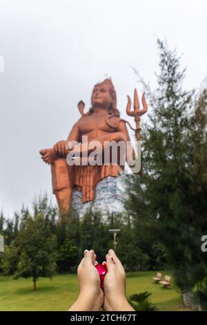 Main de prière de dévot avec des fleurs et dieu hindou flou lord shiva statue à l'image du matin est prise à la Statue de la croyance ou Vishwas Swaroopam nathd Banque D'Images