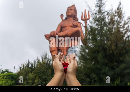 Main de prière de dévot avec des fleurs et dieu hindou flou lord shiva statue à l'image du matin est prise à la Statue de la croyance ou Vishwas Swaroopam nathd Banque D'Images