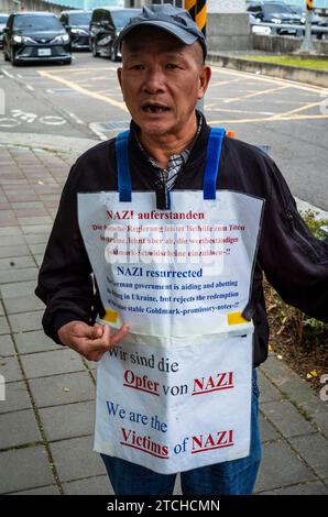 Taipei. 13 décembre 2023. Un manifestant se tient debout avec un drapeau arboré du symbole nazi devant l'école européenne de Taipei, Taiwan, le 13/12/2023, exigeant du gouvernement allemand d'honorer les obligations émises au Japon en réparation de la première Guerre mondiale La Old German Mark Association, composée de descendants de Taïwanais qui ont acheté ces obligations pendant la domination coloniale japonaise, affirme que malgré le refus des gouvernements allemand et japonais de racheter les obligations, leur valeur financière et historique reste selon Wiktor Dabkowski Credit : dpa/Alamy Live News Banque D'Images