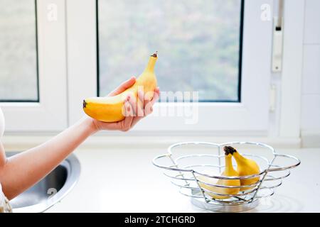 Main de femme tenant banane, collation et concept sain. Mise au point sélective sur les mains avec arrière-plan flou et espace de copie Banque D'Images