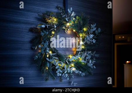 Guirlande de Noël forgée diy pin et eucalyptus, avec guirlande lumineuse, accrochée à la porte qui s'ouvre. Banque D'Images