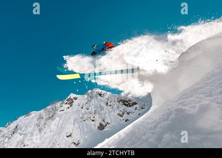 Skieur professionnel saute du banc de neige avec queue de neige poudreuse haut dans les montagnes Banque D'Images