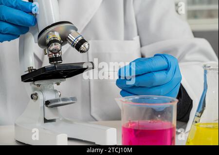 Gros plan de la main d'un scientifique portant des gants bleus et utilisant un microscope Banque D'Images