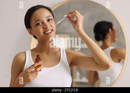 Femme souriante appliquant du sérum sur son visage dans la salle de bain Banque D'Images