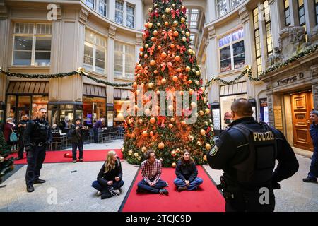 Leipzig, Allemagne. 13 décembre 2023. Des policiers se tiennent autour des membres du groupe de protestation "dernière génération" devant un sapin de Noël pulvérisé de peinture dans le passage Mädler de Leipzig. L'action a eu lieu simultanément dans plusieurs villes. Crédit : Jan Woitas/dpa/Alamy Live News Banque D'Images