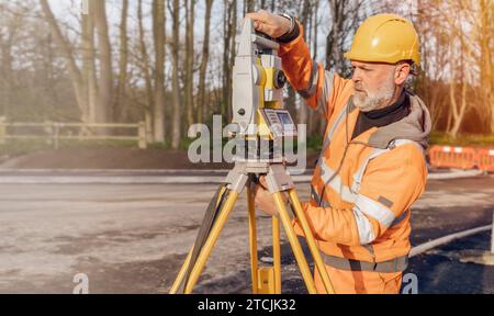 Ingénieur de chantier réglant son instrument pendant les travaux routiers. Constructeur installant le tachymètre de station de positionnement total sur le chantier de construction pour la nouvelle route setti Banque D'Images