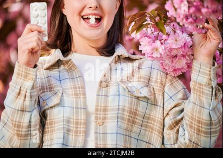 Femme allergique souffrant d'allergie saisonnière au printemps. Vue rognée de la jeune femme appliquant la pilule d'allergie, posant dans le jardin en fleurs au printemps. Concept de médication antihistaminique Banque D'Images