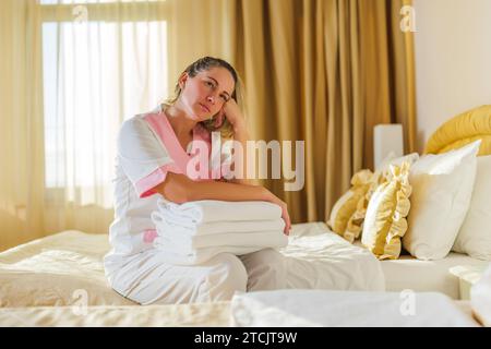 Image d'une femme de chambre triste surmenée assise sur le lit dans une chambre. Banque D'Images