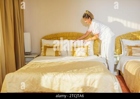 Belle femme de chambre faisant le lit dans une chambre. Banque D'Images