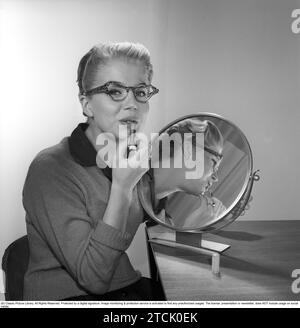 Dans les années 1950 Une jeune femme avec un miroir mettant du rouge à lèvres. Elle a les lunettes et les arcs typiques des années 1950 1958. Kristoffersson réf. CB99-11 Banque D'Images