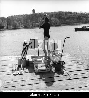 style de vie des années 1950. Une jeune femme au soleil portant un maillot de bain. Dans l'image, il y a beaucoup d'objets opportuns en plastique qui étaient populaires à l'époque. Surtout lorsque vous êtes en vacances d'été ou en camping. Un cas pratique pour les transporter. 1958 Kristoffersson réf DB96-11 Banque D'Images