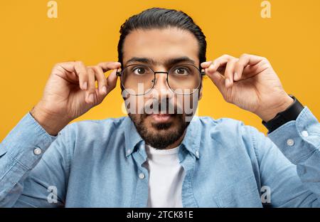 Homme sérieux ajustant des lunettes rondes élégantes, portant une chemise en denim bleu Banque D'Images