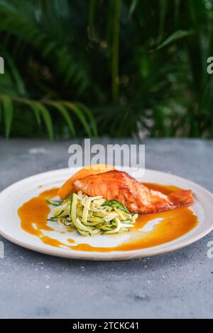 Steak de saumon avec nouilles de courgettes avec sauce orange et orange sur une assiette blanche Banque D'Images