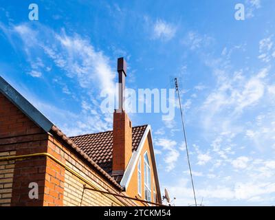 toit carrelé de maison de village en brique avec cheminée allongée, antenne et ciel bleu avec des nuages cirrus blancs en arrière-plan sur la journée ensoleillée d'automne Banque D'Images