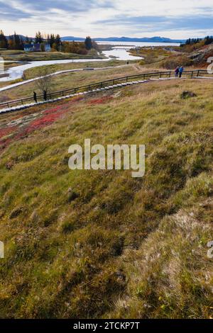 Islande, cercle d'Or, Parc National de Thingvellir aux couleurs de l'automne. Le rift médio-atlantique entre les plaques tectoniques nord-américaine et eurasienne. Almannagja gorge marquant le bord de la plaque tectonique nord-américaine, avec des touristes touristiques. Lac Thingvallavtn sur la crête de Reykjares dans la vallée du Rift au-delà. Banque D'Images