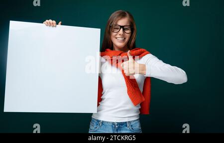 Mignon jeune femme dans des lunettes tient une planche et montre des tâches d'affaires sur elle Banque D'Images