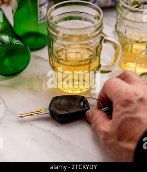 Un concept de conduite de boissons avec une table pleine de boissons alcoolisées et une personne ramassant un jeu de clés de voiture pour conduire. Banque D'Images