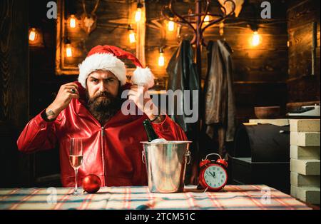 Père Noël barbu masculin brutal avec horloge et champagne pour rencontrer le nouvel an. Magnifique décor de Noël et lumières Banque D'Images