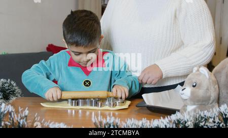 Maman et fils faisant des biscuits. Rouleau à pâtisserie garçon sur les emporte-pièces. Photo de haute qualité Banque D'Images