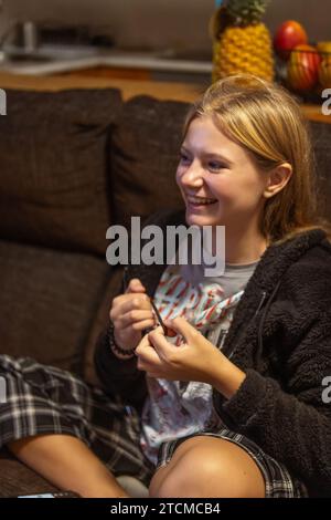 Heureuse adolescente d'apparence légère se trouve sur un canapé sombre dans la chambre, photo.enfance heureuse verticale Banque D'Images