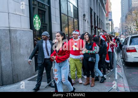 Des centaines de Santas, accompagnés de leurs assistants et de quelques elfes coquins, attendent en ligne pour entrer dans le Smith Bar dans le quartier Nomad de Manhattan à New York lors du bar crawl annuel, SantaCon le samedi 19 décembre 2023. SantaCon, principalement un bar crawl dans le Père Noël et d'autres costumes liés à Noël, attire les masqueradeurs qui vont de bar en bar. (© Richard B. Levine) Banque D'Images