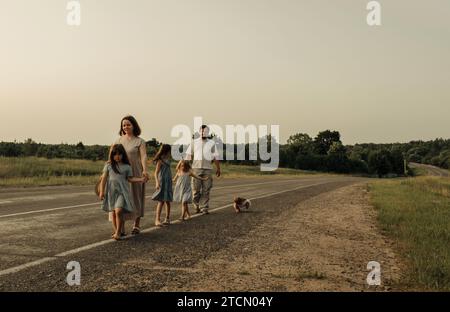 Maman, papa et filles marchent l'un après l'autre le long d'une route rurale le long de la forêt. Une famille heureuse Banque D'Images