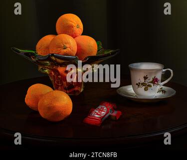 Oranges dans un plat et une tasse de café en porcelaine et une barre de chocolat sur la table. Banque D'Images