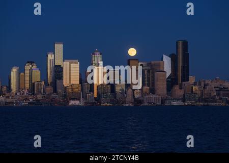 Seattle, WA, États-Unis - 28 octobre 2023 ; Hunter's Moon se lève derrière les gratte-ciel du centre-ville de Seattle et Elliott Bay avec des bâtiments qui brillent au coucher du soleil Banque D'Images