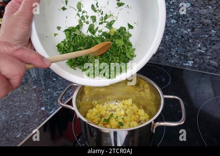 Préparation d'une soupe de cresson, cresson frais dans un bol, palette d'agitation, cuillère en bois, casserole avec des morceaux de pommes de terre, cuisinière à induction, plaque vitrocéramique Banque D'Images