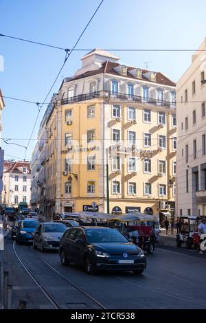 Une journée animée à Lisbonne : vue à angle bas d'un bâtiment jaune vibrant, au milieu du tumulte et de l'agitation des voitures et des tramways Banque D'Images