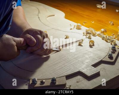 Artisan luthier fabricant d'instruments à cordes sculpte une plaque arrière de violoncelle en bois d'épicéa avec gouge à Crémone Italie Banque D'Images