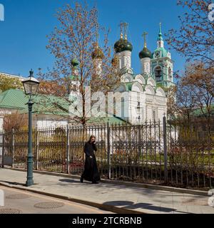 Jeune homme vêtu d'une robe noire marche près de l'église de la décapitation de Jean le Baptiste par Bohr tout en parlant sur son téléphone portable. Moscou, Russie. Banque D'Images