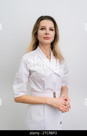 Portrait vertical de jolie femme médecin portant un uniforme de manteau debout sur fond blanc isolé bras croisés. Portrait de studio de jeune femme Banque D'Images