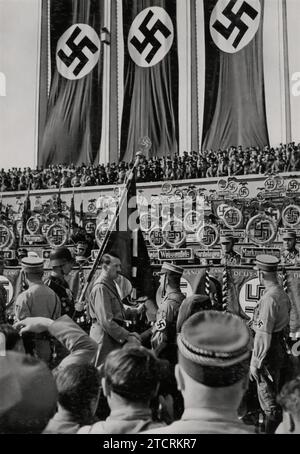 Au cours du Reichsparteitag (rassemblement du parti nazi) de 1934, Adolf Hitler est capturé dans un moment significatif, serrant la main d'un soldat lors de la cérémonie de la consécration des normes. Cet événement symbolisait l'unité et la loyauté des forces armées envers le régime nazi. L'implication personnelle d'Hitler, comme en témoigne la poignée de main, souligne son rôle central dans ces démonstrations de pouvoir et la culture délibérée d'un lien entre le parti et l'armée. Banque D'Images