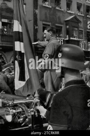 Au rassemblement de Nuremberg, Adolf Hitler est vu saluant le «Blutfahne» (drapeau du sang) de 1923, un symbole vénéré dans les traditions nazies. Ce drapeau, taché du sang des membres du parti du putsch de la Beer Hall, a été utilisé pour consacrer de nouveaux drapeaux. Le salut d'Hitler au Blutfahne souligne la vénération du régime pour ses luttes initiales et les sacrifices de ses membres, symbolisant un fil continu de loyauté et de martyre au sein du mouvement nazi. Banque D'Images