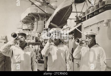 L'image montre les Marines allemands de la Kriegsmarine engagés dans un rituel de communication crucial à bord d'un navire : jouer de la trompette pour signaler le «rassemblement pour le service» à tous les soldats à bord. Cette pratique faisait partie intégrante de la vie sur les navires de la marine allemande pendant la Seconde Guerre mondiale, servant de repère auditif pour les marines de se rassembler pour le service ou les annonces importantes. Banque D'Images