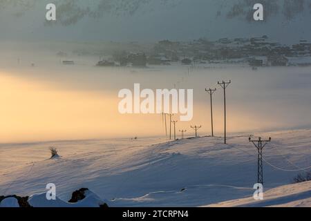 Un village couvert de brouillard et de neige et les fils électriques atteignant le village Banque D'Images