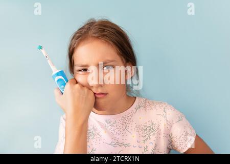 une femme triste et bouleversée tient une brosse à dents dans sa main, debout sur un fond bleu et regardant avec déception la caméra, tenant sa main sur son che Banque D'Images