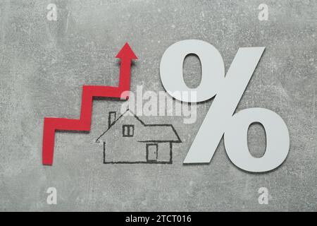 Augmentation du taux hypothécaire illustrée par une flèche ascendante, une icône de maison et un signe de pourcentage sur fond gris, vue de dessus Banque D'Images
