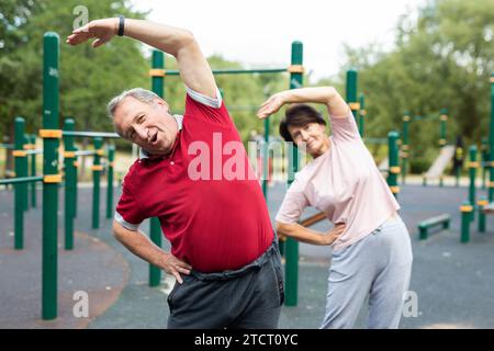 Couple de famille mature en vêtements de sport faisant de la gymnastique ensemble à la salle de gym en plein air Banque D'Images