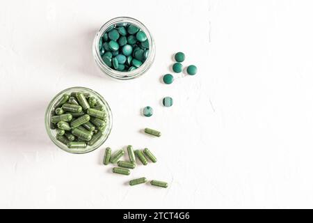 Deux bocaux en verre remplis de capsules et de comprimés de spiruline biologique sur fond blanc texturé. Vue de dessus. Nettoyage naturel du corps. Banque D'Images