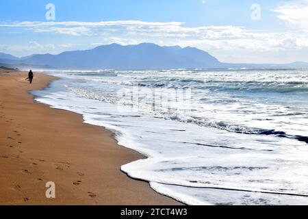 Silhouette d'une seule personne dans la distance marchant seule le long de la plage vide naturelle sur une journée ensoleillée avec des vagues mousseuses blanches entrant, Grèce, Europe Banque D'Images