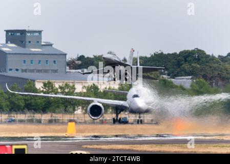 USAF Lockheed Martin F-16C Fighting Falcon décollant de l'aéroport de Farnborough avec un avion de ligne moderne et des bâtiments historiques dans la brume de chaleur d'efflux de jet Banque D'Images