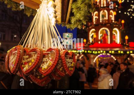 Bonn, Allemagne - 6 décembre 2023 : coeurs traditionnels en pain d'épice accrochés à un marché de Noël festif avec fond flou de carrousel illuminé. Banque D'Images