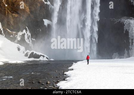 Femme avec veste rouge debout devant la cascade Skogafoss Banque D'Images