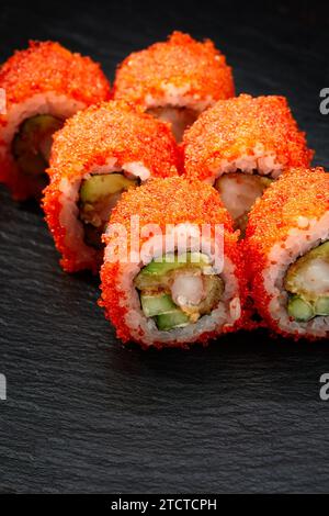 Les sushis roulent la californie avec du crabe des neiges, du fromage à la crème, du concombre, des graines de sésame et du caviar macago sur fond noir avec reflets. Menu de sushis, japonais Banque D'Images
