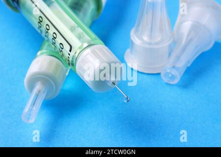 Gros plan goutte de médicament à l'extrémité d'une aiguille d'un stylo de seringue d'insuline sur un fond bleu Banque D'Images