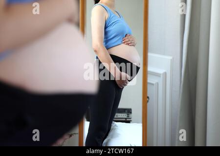 Femme enceinte regardant son ventre devant un miroir en pied Banque D'Images