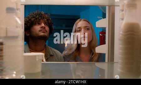 Point de vue POV à l'intérieur du réfrigérateur fille caucasienne femme petite amie femme et homme arabe gars indien petit ami mari multiracial couple la nuit Banque D'Images